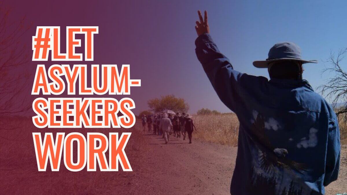 A photo with a group of asylum workers, at the back is a group and the front is one person with a peace sign on their left hand. On the left of the poster in orange writing is, "#Let Asylum-Seekers Work." 