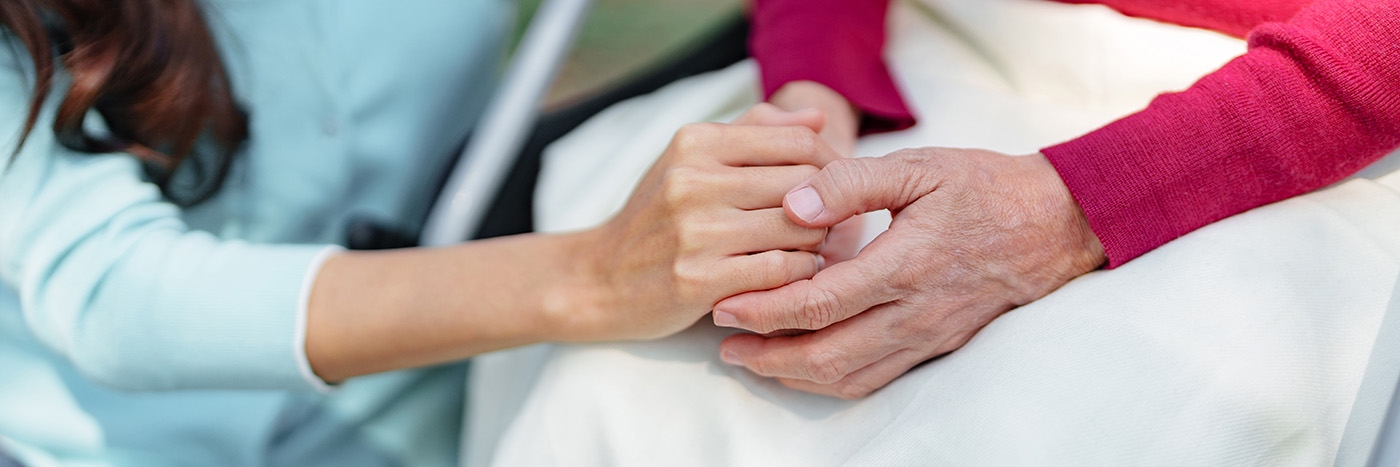 a young woman clasps hands with an older woman in a comforting gesture.