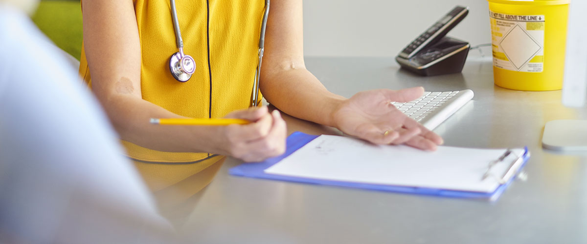 Adult wearing stethoscope with clipboard on table.