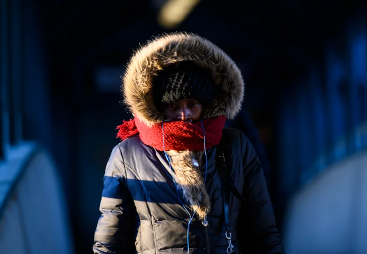 A woman walks on a pedestrian bridge with her face covered to protect from the cold.