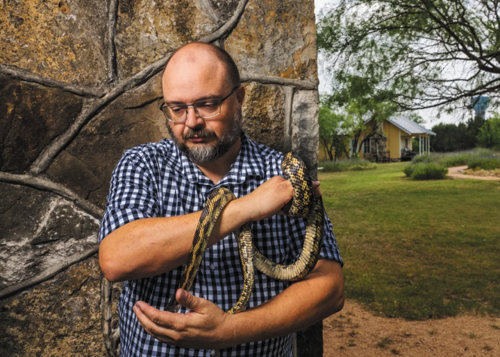 A man holds a snake that is partially coiled around his arm.