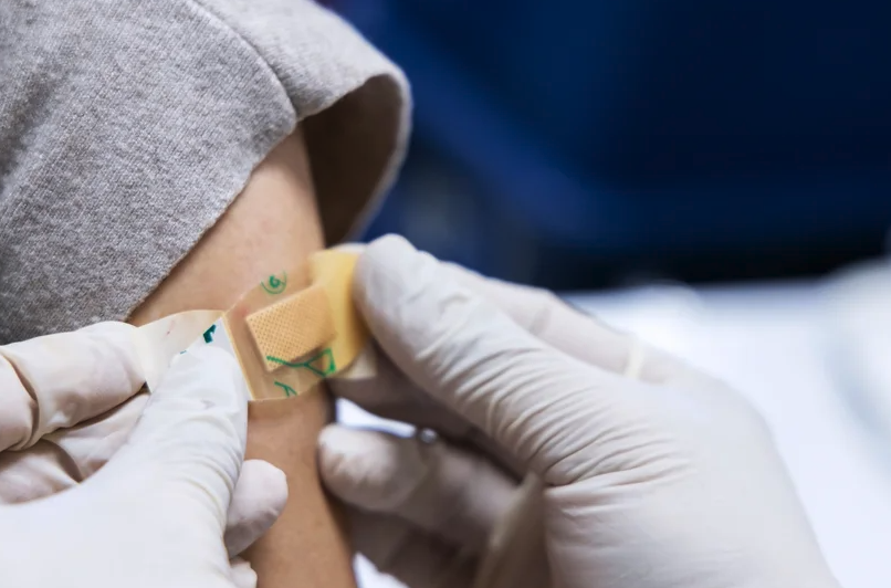 Close-up of a gloved doctor placeing a bandaid on a person's arm