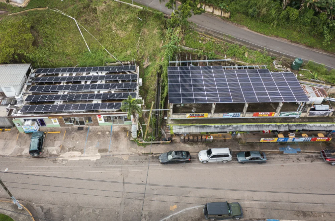 photo of several roof-top solar panels, atop storefront buildings nestled against a small hillside, that power a local microgrid network in Puerto Rico 