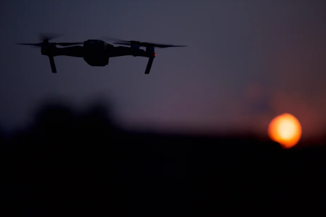 A photo of a shadowed drone on a dark horizon, near setting sun