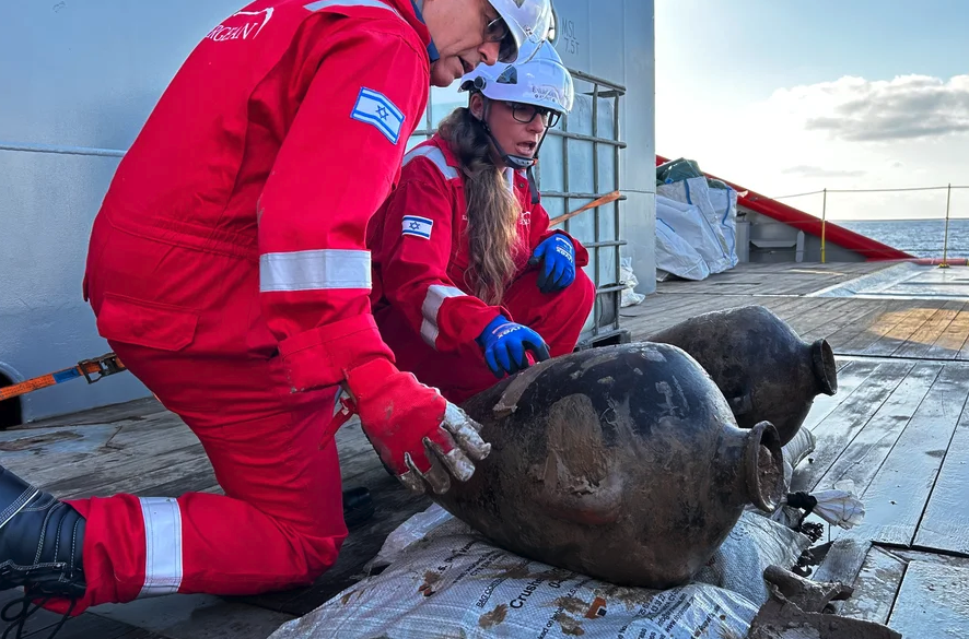 Researchers examine two large urns on the deck of a ship
