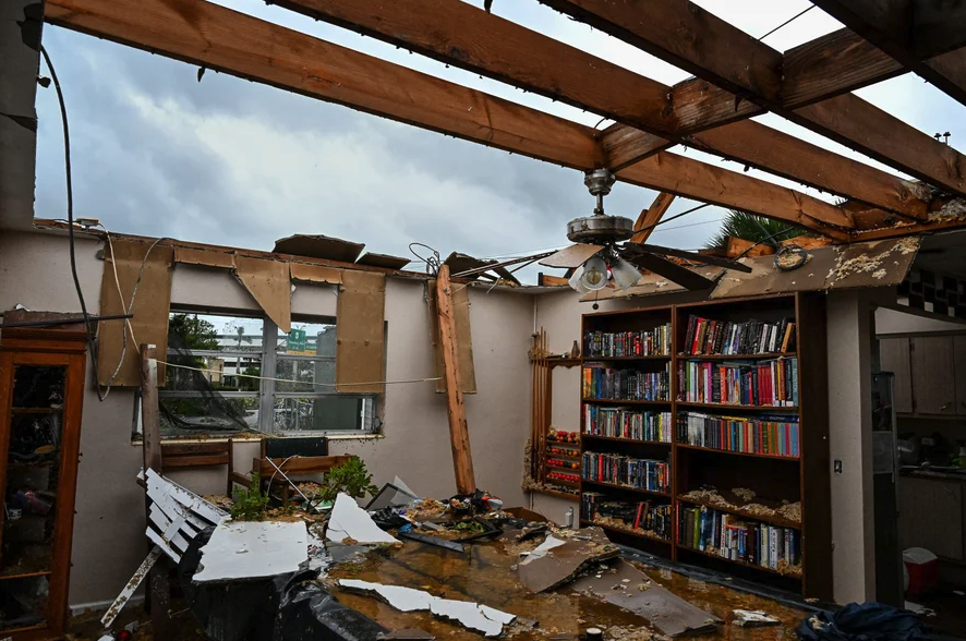 A home is missing its roof except for beams, as seen from inside