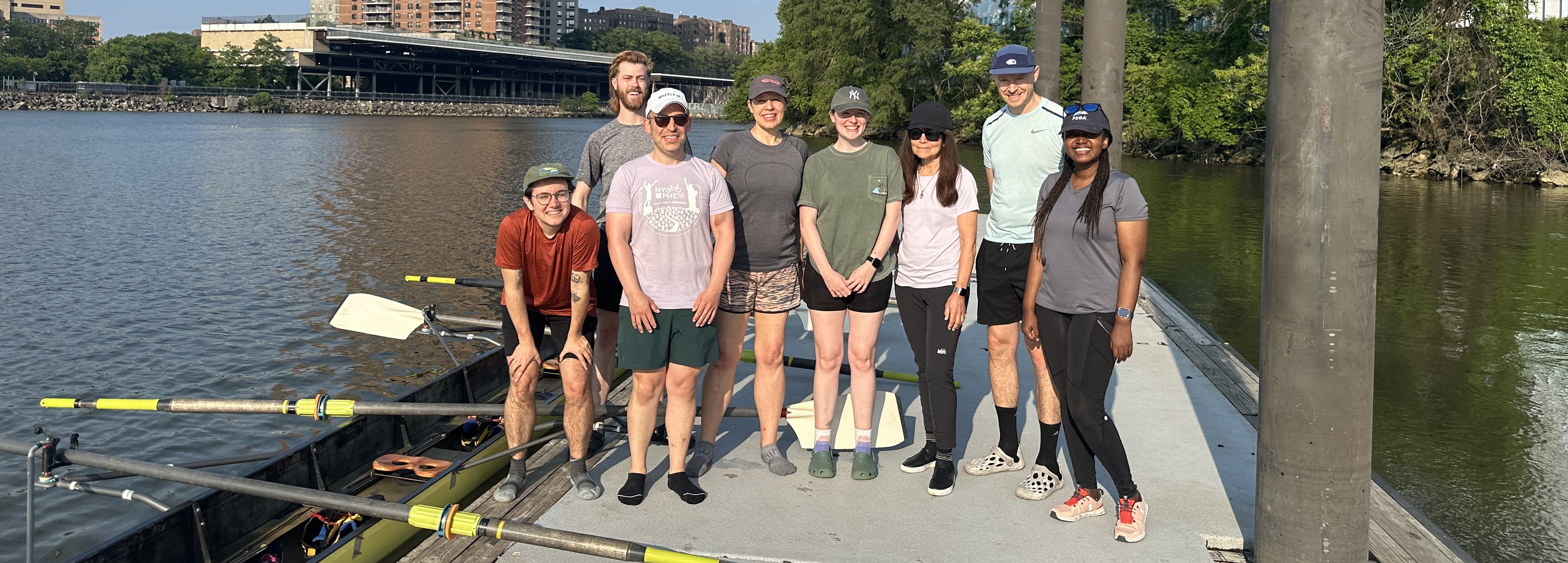 Image of eight rowers standing on a dock next to a rowing shell.