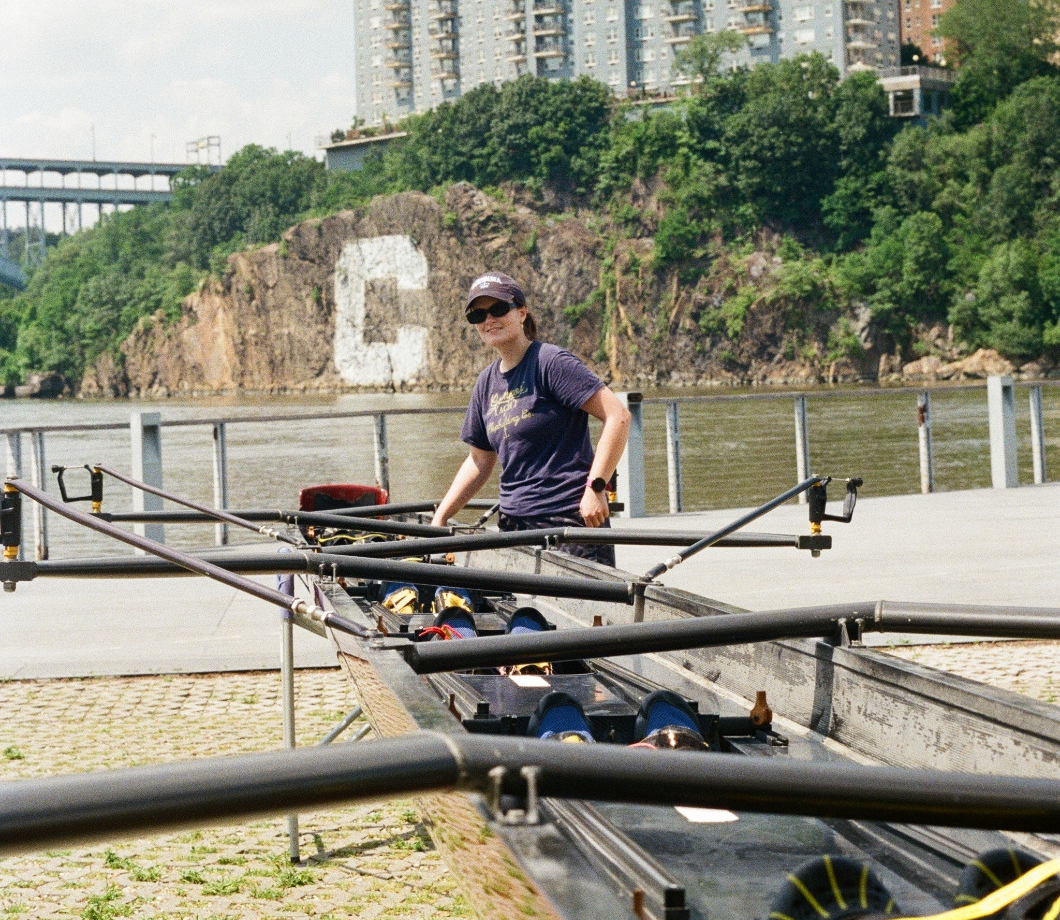 A rower stands next to an eight-person shell in slings, installing a foot stretcher.