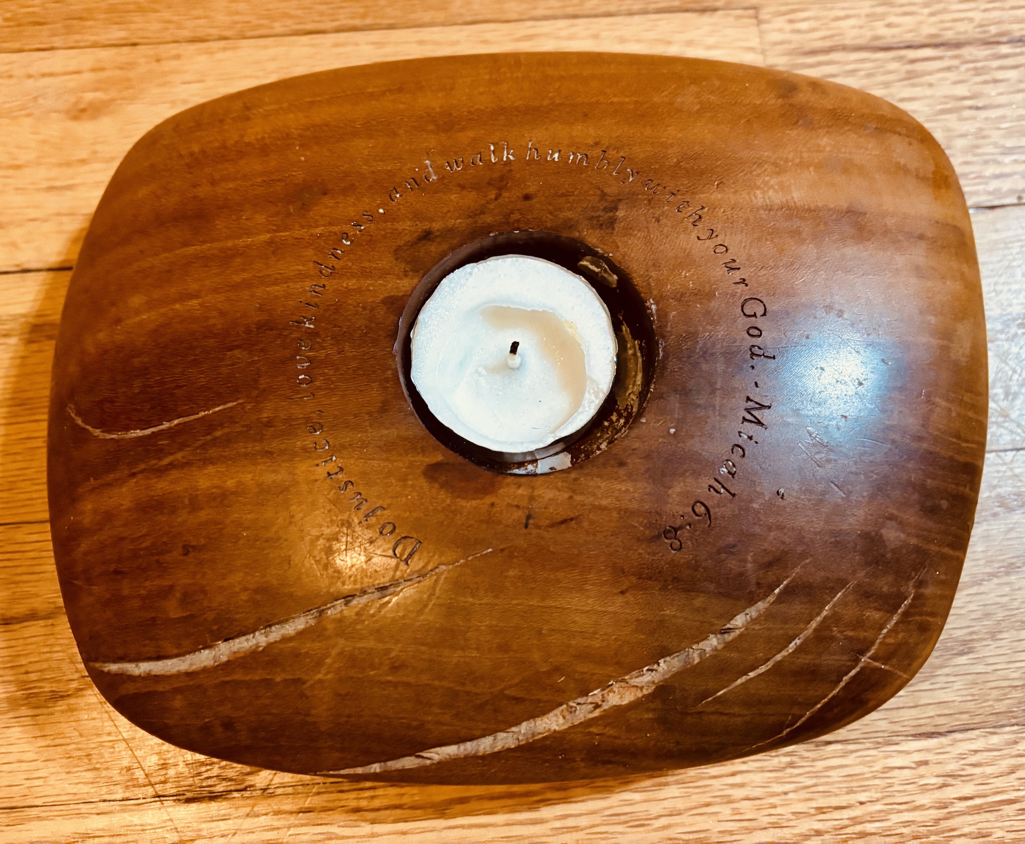 A wooden chalice with splits and the words 'This is what you shall do: act justly, love mercy, and walk humbly with your god.' etched around the candle.