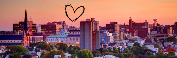 A view of downtown Portland, Maine at sunset with an outline of a heart in the top center.