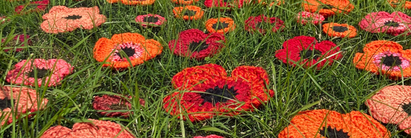 Multicolored crocheted flowers strewn across a green grass field - an art installation at Park Hill Orchard, Easthampton MA.