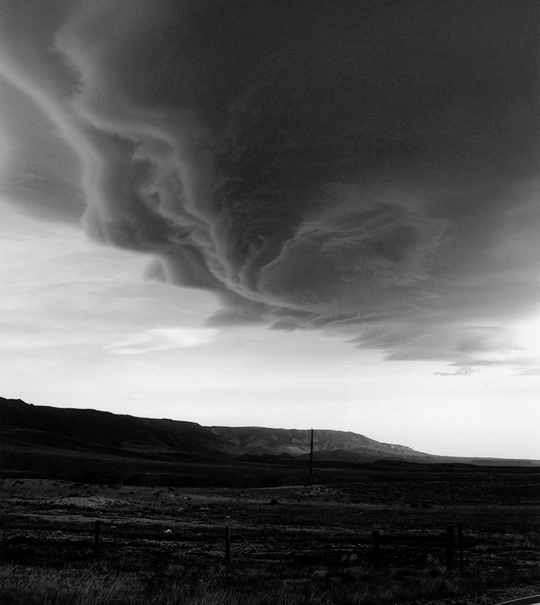 Sparsely vegetated land with hills in the background under a large, ominous, swirling cloud.