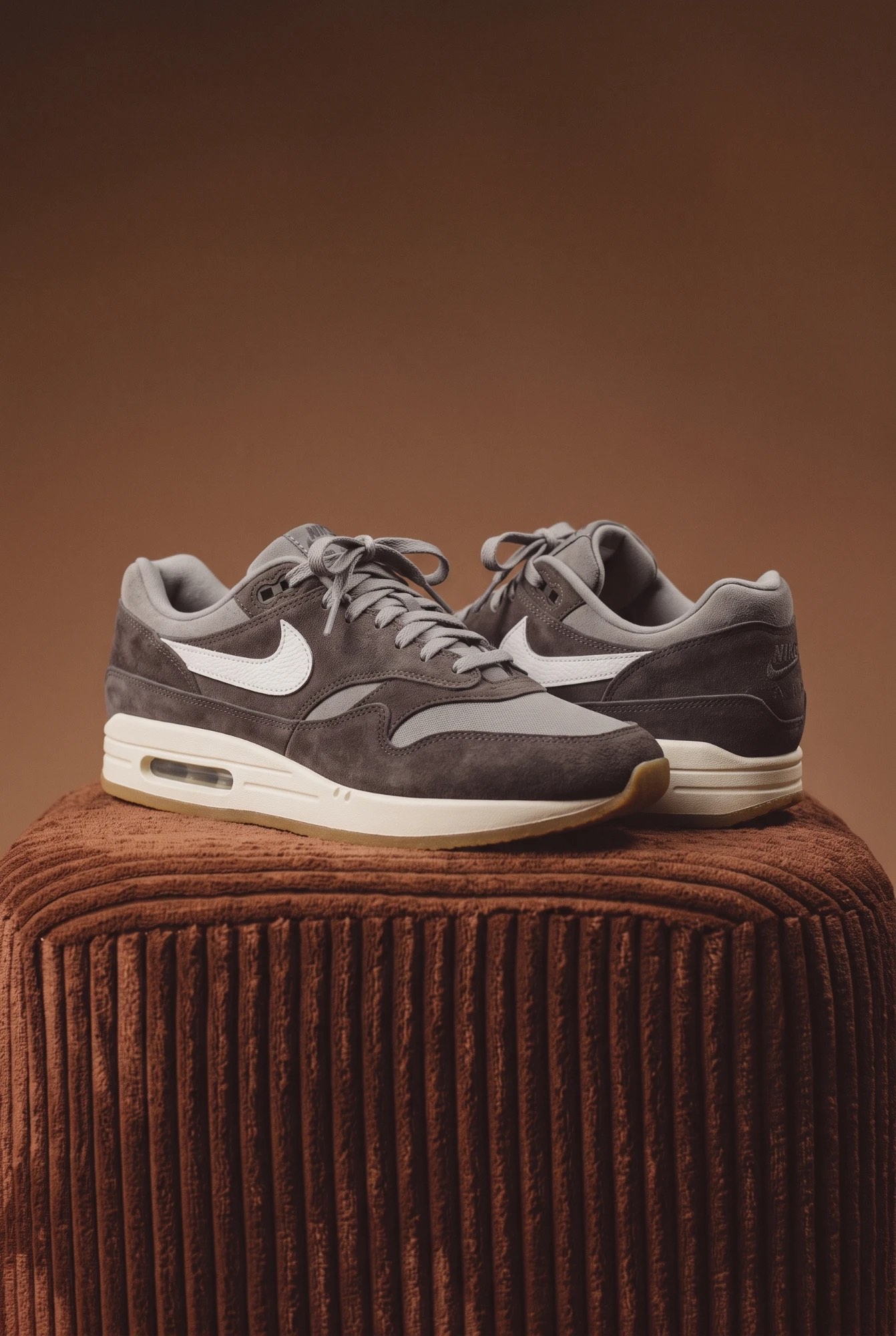 Nike Air Max 1 Crepe Soft Grey on a brown corduroy pedestal